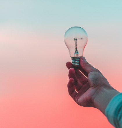 Hand holds lightbulb up to setting sun in sky